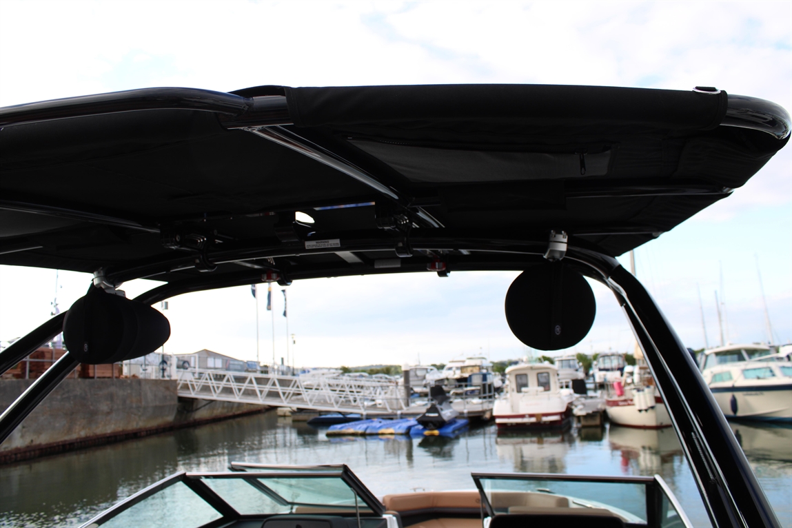 View from a boat canopy overlooking a marina, with various boats docked and a calm water surface reflecting the sky.